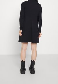Abito nero a maniche lunghe con silhouette svasata, realizzato in un morbido tessuto, abbinato a stivali neri alla caviglia con suola spessa e linguette.