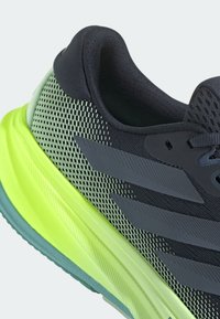 Gros plan d'une chaussure de course noire et vert néon avec tige en mesh à motifs et semelle amortie.
