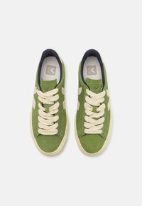 Green suede sneakers with cream laces, white accents, and a navy collar. Features a logo on the tongue and a textured sole.