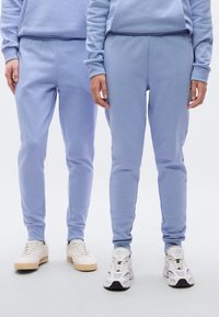 Ανοιχτό μπλε φόρμα με ελαστική μέση και στενό τελείωμα στα πόδια. Απαλό υλικό από βαμβακερό μείγμα, σε συνδυασμό με λευκά αθλητικά παπούτσια.