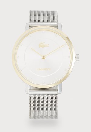 Montre-bracelet ronde avec un cadran blanc, des accents dorés et un bracelet en maille argentée. Présente un logo doré et des marqueurs en cristal sur le cadran.