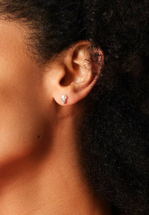 Perle stud ørering med en lille glitrende accent, sat i et sølvfarvet metal. Fokuser på den runde perle og den delikate, intrikate detaljering.