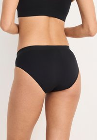 Mutande nere in cotone a vita alta con una texture liscia, bordi senza cuciture e design minimalista, dotate di un ampio bordo in vita per il massimo comfort.