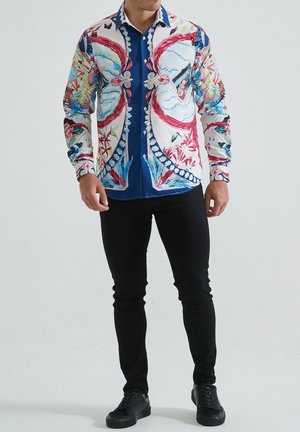 Chemise à manches longues à motifs floraux en tissu bleu et blanc, avec des motifs colorés et un col boutonné. Assortie avec un pantalon noir et des chaussures.