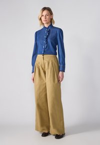 Denimbluse med volangkrage og knaplukning foran, parret med højtaljede khaki bukser. Brune loafers fuldender outfittet.