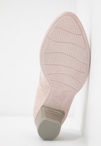 Bottine en daim rose clair avec une semelle en caoutchouc texturée, dotée d'un bout arrondi et d'un talon empilé bas. Motif en relief notable sur la semelle.