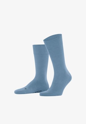 Para prostych niebieskich skarpetek do kostek stojących pionowo na białym tle.