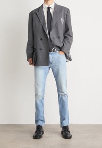 Šedé s proužky, dvouřadé sako, bílé košile, černá kravata, světle modré džíny a černé boty. Sako má kapsu a jemný detail s logem.