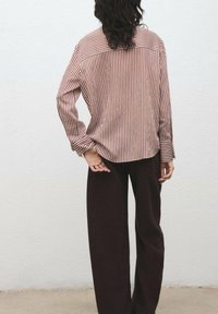 Striped long-sleeve shirt in red and white with a rounded hem paired with dark brown wide-leg pants. Subtle texture and relaxed fit.