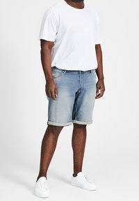 Shorts de mezclilla azul claro con dobladillos enrollados, que presentan un corte relajado. Combinados con una camiseta blanca de cuello redondo y zapatillas blancas.