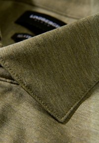 Olivgrünes Hemd mit Kragen aus strukturiertem Stoff, mit leicht tailliertem Kragen und sichtbaren Nahtdetails. Markenzeichen sind sichtbar.