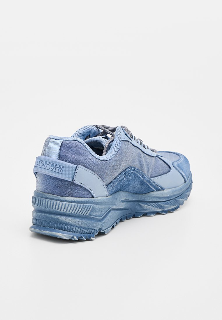 Zapatilla azul claro con paneles de tela mixta y ante, suela texturizada, cuello acolchado y tirante con marca en el talón.