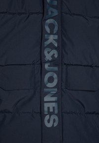 Giubbotto puffer blu navy con design trapuntato, due tasche frontali e stampa del logo verticale in una tonalità più chiara sul davanti.