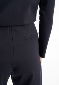 Indumento fitted nero realizzato in un tessuto liscio e elasticizzato. Presenta una tasca laterale e un design elegante, che mostra linee pulite e una minima decorazione.