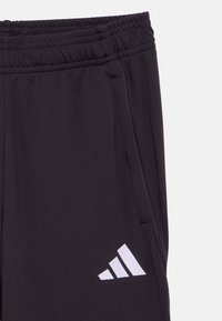 Černé sportovní kalhoty s elastickým pasem, bočními kapsami a bílým logem Adidas. Hladká struktura látky s minimem švů.