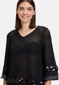 Schwarzes gestricktes Oberteil mit V-Ausschnitt und dreiviertellangen Ärmeln. Verfügt über ein lockeres Häkelmuster und Paillettenakzente am Saum.