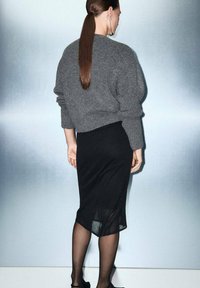 Suéter gris de punto con un ajuste holgado, combinado con una falda negra hasta la rodilla hecha de un tejido transparente. Muestra un estilo suave y minimalista.