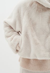 Luddig, kortärmad beige hoodie med en mjuk textur, som har en fodrad huva och en lager på lager, ljusare beige nederkant.