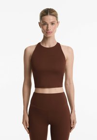 Top scurt maro, fără mâneci, cu un gât înalt și o textură netedă, asortat cu colanți maro cu talie înaltă, având un design fără cusături.