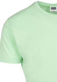 Lys grønne bomulds T-shirt med rund hals, korte ærmer og synlige syninger. Etiketten siger "URBAN CLASSICS," størrelse S.