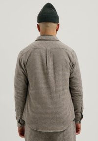 Camicia a quadri con colletto, tonalità di marrone chiaro e grigio, maniche lunghe e vestibilità comoda, indossata con un berretto scuro.