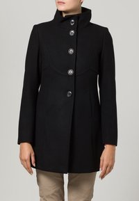 Svart ullkappa med hög krage, sex framträdande knappar, skräddarsydd passform och slät textur. Har böjda sömdetaljer på framsidan.