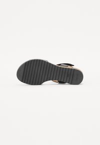 Black sandal sole with horizontal grooves for grip, featuring a brown leather strap attached to a solid black base.