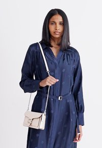 Navy dress with button front, subtle pattern, and a belted waist. Model holds a small cream handbag with a chain strap and clasp detail.