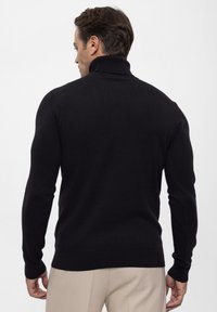 Zwarte, geribbelde turtleneck sweater met een getailleerd ontwerp en lange mouwen, gemaakt van een gladde brei stof. Geen zichtbare patronen of logo's.