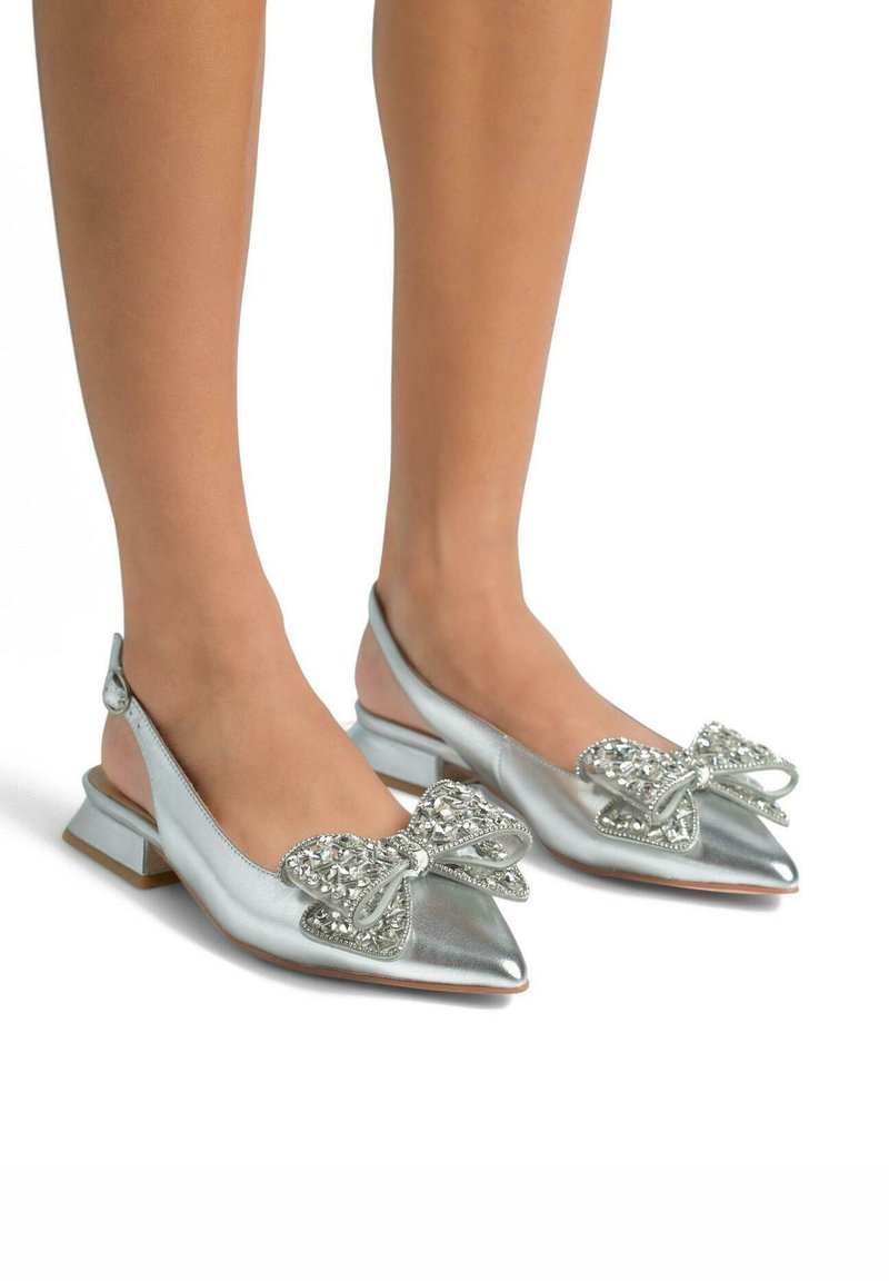 Des ballerines argentées à strap arrière présentent un bout pointu, une texture en cuir métallisé et un nœud décoratif avec des accents en cristal à l'avant.
