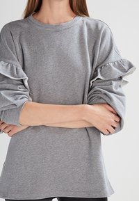 Grå sweatshirt med volangärmar och kontrasterande kant, rund halsringning, mjuk textur och lös passform.