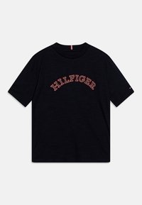 Camiseta negra de algodón, con un logo bordado en rojo de "HILFIGER" en diseño de arco en la parte frontal. Mangas cortas, cuello redondo.