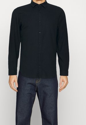 Chemise noire à manches longues, à boutons, en tissu doux et texturé, avec un col, des boutons à l'avant et un ourlet arrondi, assortie à un jean en denim foncé.
