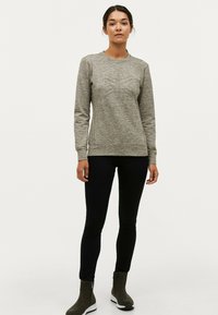 Grå tekstureret sweatshirt med et geometrisk design foran, parret med mørke jeans og ankelstøvler. Simple rund halsudskæring og lange ærmer.