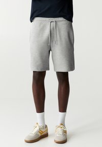 Graue Baumwollshorts mit einem elastischen Bund und Kordelzugdetail. Kombiniert mit beigen Sneakers mit orangen Akzenten und weißen Socken.