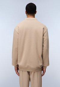 Felpa beige con vestibilità rilassata, collo e polsini a costine e tessuto testurizzato. Superficie liscia senza motivi visibili o accessori.