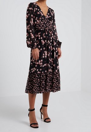 Sort blomsterkjole med lange ærmer, V-udskæring og en flæseforing. Mønstret indeholder lyserøde blomster på et struktureret stof. Sorte højhælede sandaler.