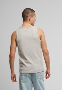 Lysegrå ribbet tanktop med scoop halsudskæring, designet uden synlig branding, parret med lyseblå denim bukser. Bagfra.