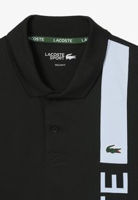 Polo shirt nera con colletto, dotata di striscia laterale azzurra, logo Lacoste e scritta "LACOSTE SPORT" stampata in bianco. Vestibilità regolare.