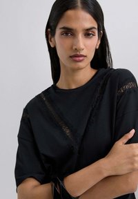 Camiseta negra con encaje en el cuello y las mangas, con un corte holgado y textura de algodón suave.