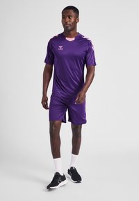 Purple athletic jersey and shorts in a lightweight fabric, featuring pink detailing on shoulders and branding on the chest. Black sneakers worn.