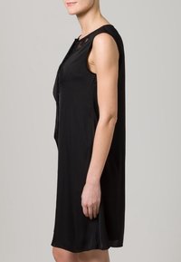 Vestito nero senza maniche con scollatura rotonda, silhouette fluida e delicati dettagli in pizzo sulle spalle. Tessuto dalla consistenza morbida.