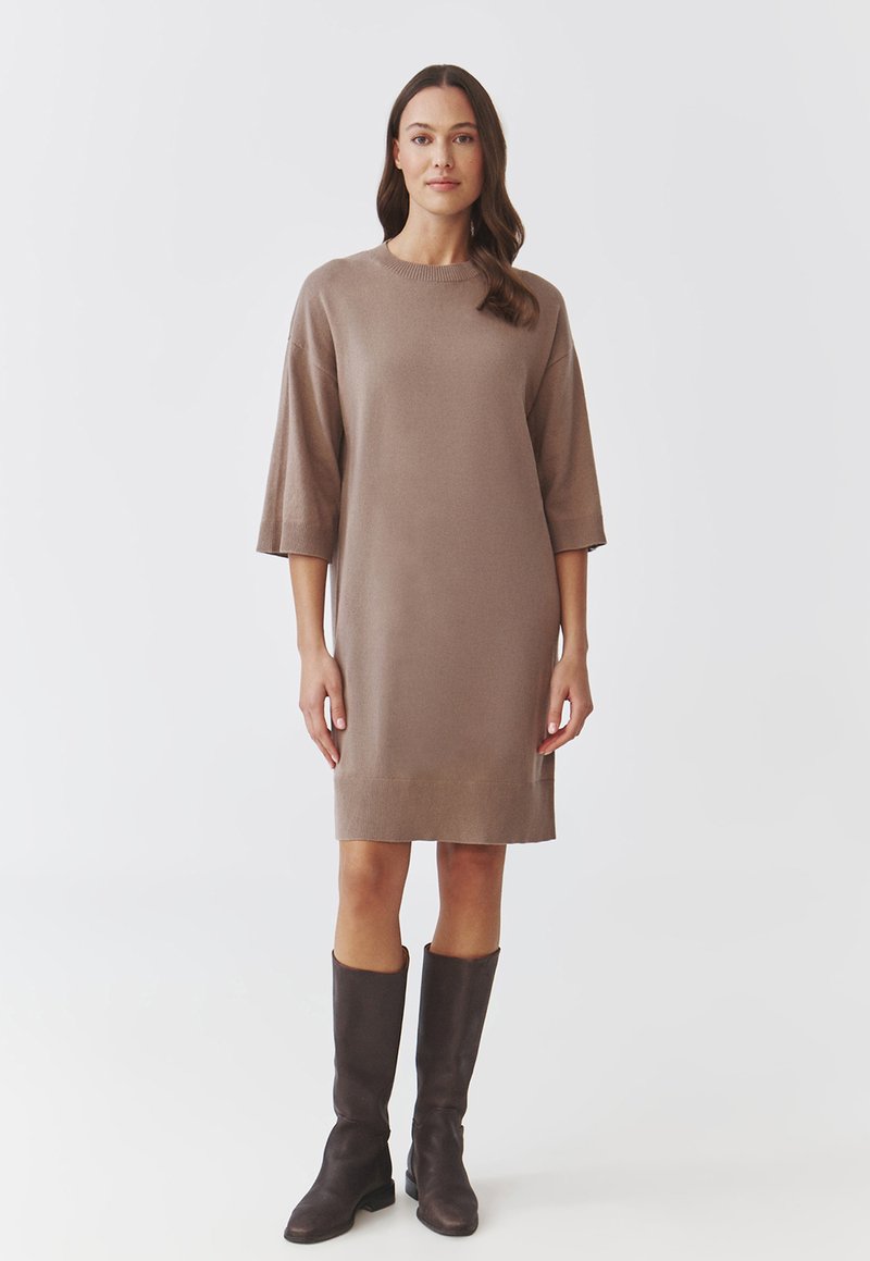 Robe en maille marron à manches courtes, coupe droite et ourlet côtelé. Associée à des bottes en cuir marron foncé jusqu'aux genoux.