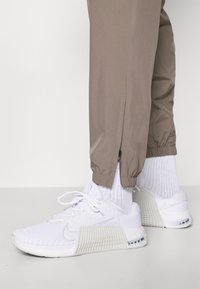 Hvide sportssko med tekstureret mesh-overdel og mønstret sål, parret med lysebrune joggers med lynlåse ved cuffs og elastisk talje.