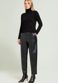 Zwarte coltrui gecombineerd met zwarte leren joggerbroek. Slim fit, gladde textuur, voorzien van zakken aan de zijkant en taps toelopende manchetten. Zwarte puntige laarzen.