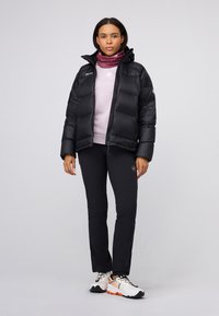 Doudoune noire rembourrée avec capuche, associée à un haut violet clair, un pantalon noir et des chaussures blanches avec des accents orange.