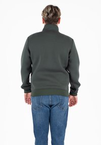 Donkergroene sweatshirt met een hoge kraag, geribbelde manchetten en zoom. Draag het met blauwe jeans, die een gladde, gestructureerde stof tonen.
