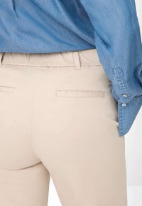 Beige pants with a smooth texture and elastic waistband, paired with a blue denim shirt. Features two back pockets with stitched edges.