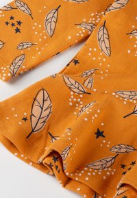 Orange fabric top featuring a leaf pattern in navy with white dots and stars. Includes long sleeves and a gathered hem for a flared look.