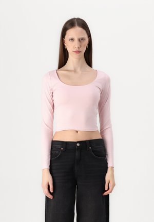 Top corto de manga larga en suave tela rosa con un escote amplio en forma de u, combinado con jeans de mezclilla negros de tiro alto.